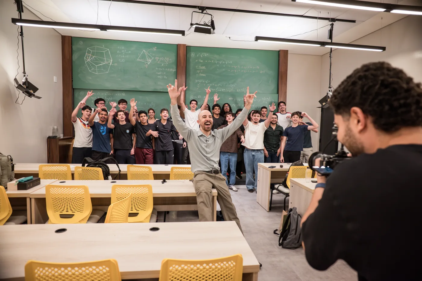 O Engenheiro comemorando de braços abertos com a turma inteira na frente do quadro, com a câmera gravando