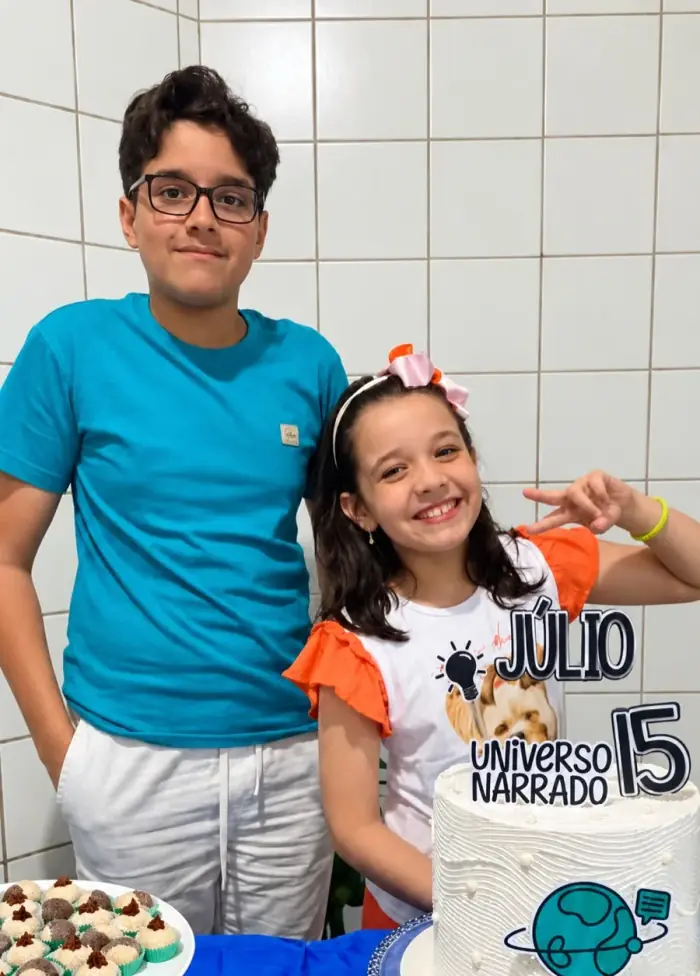 Júlio e a irmã ao lado do bolo de 15 anos com o tema do Universo Narrado